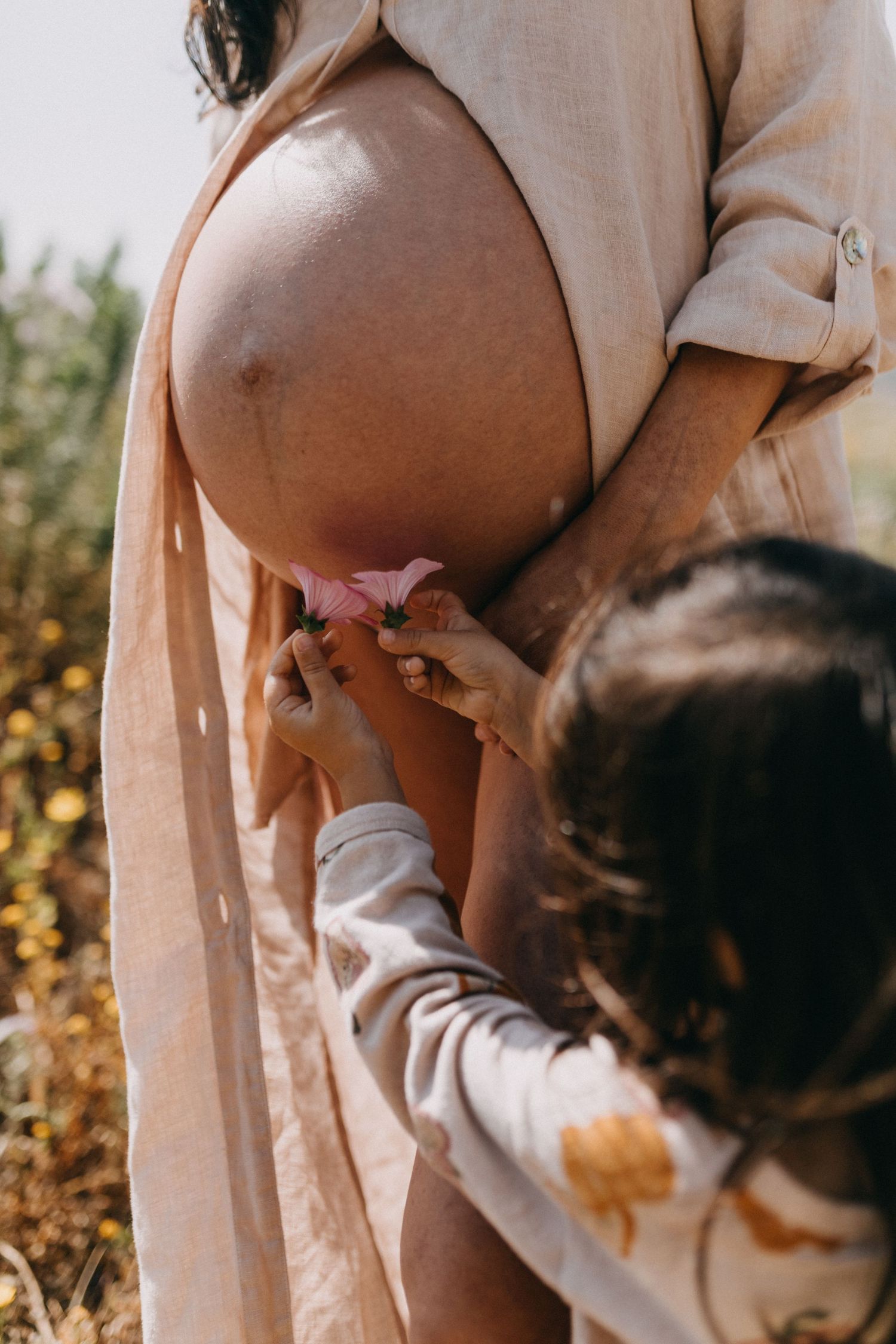 Intimate maternity moments showing small hands touching a pregnant belly in beige clothing.