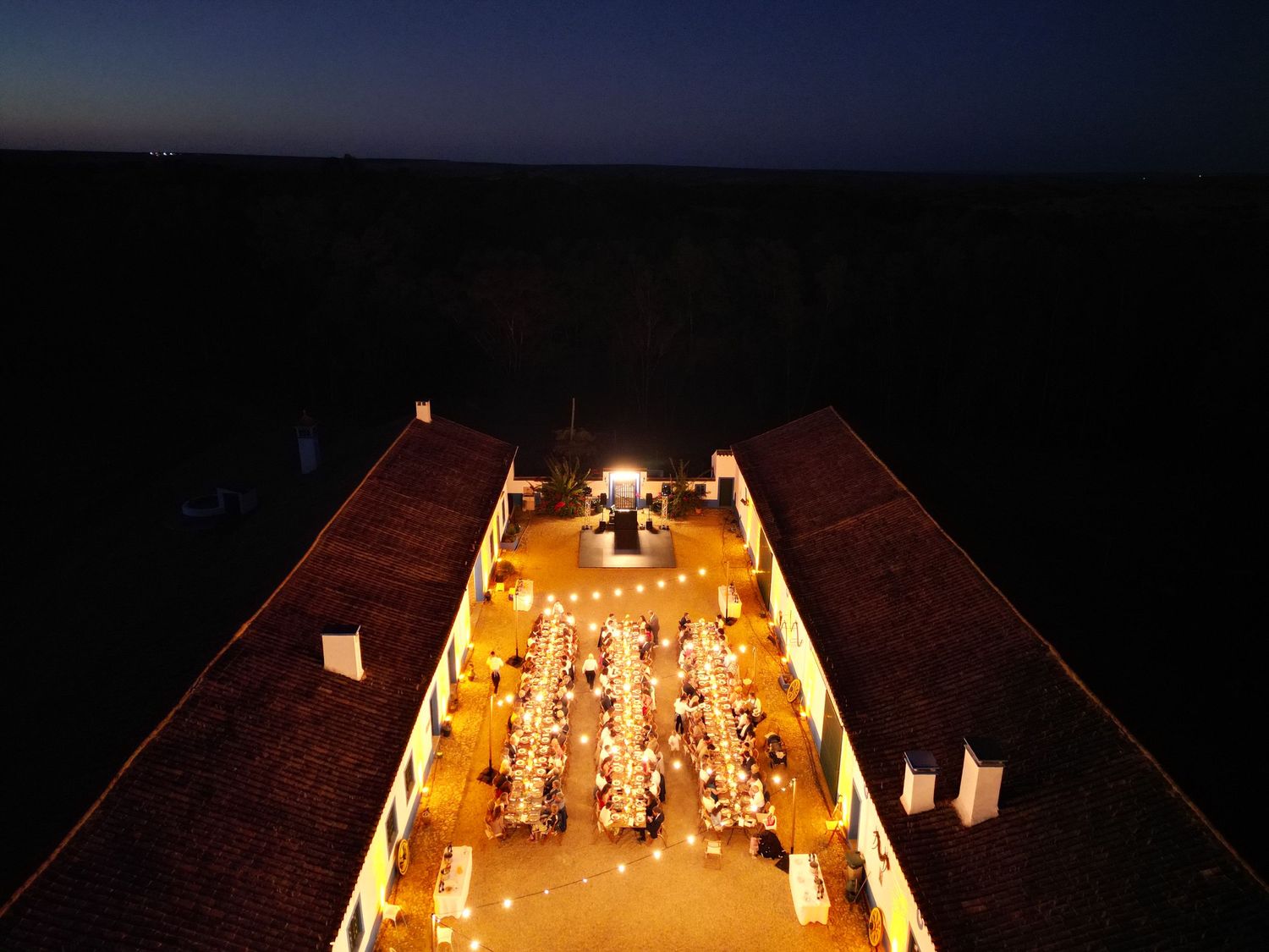 Long wooden table illuminated by warm candlelight creates an intimate dining atmosphere in a dark restaurant setting.