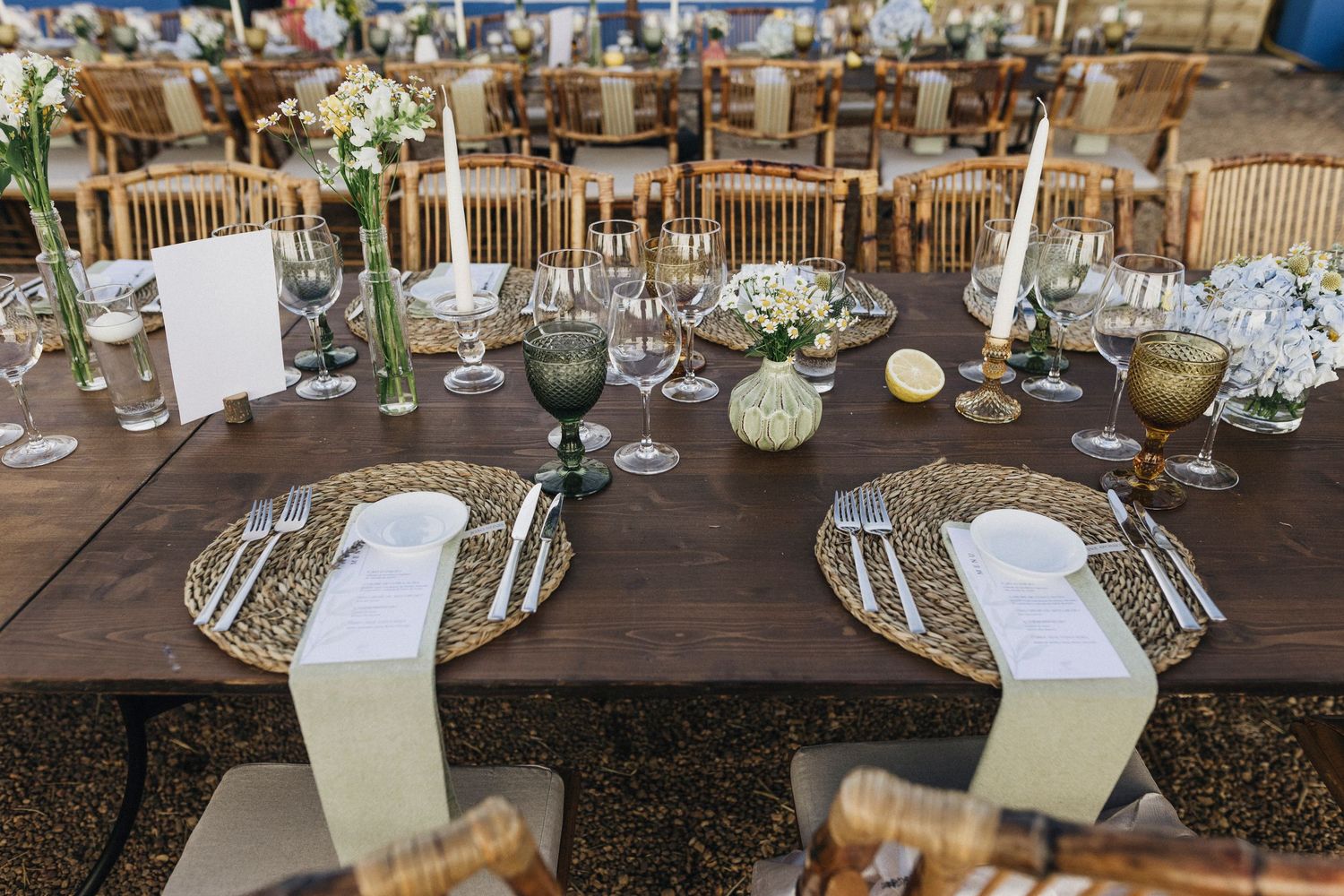 Elegant rustic wedding reception tables set with white floral centerpieces, candles and burlap runners in a barn venue.