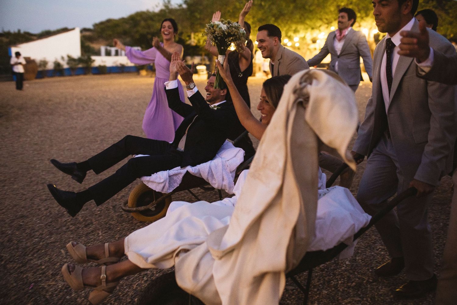 Wedding party dancing and celebrating on a rustic outdoor dance floor at sunset.