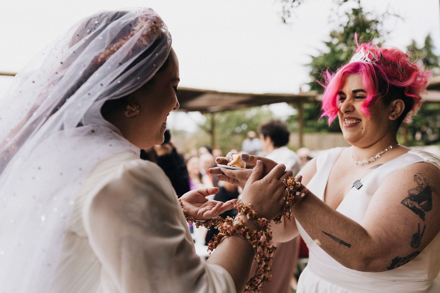 Two people in white wedding attire share an intimate moment while exchanging rings during a ceremony.