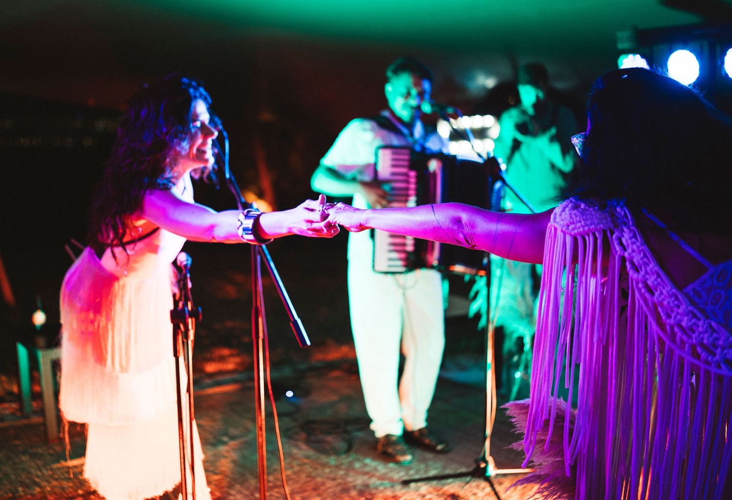 Outdoor nighttime event with colorful purple and green lighting illuminating performers and audience.