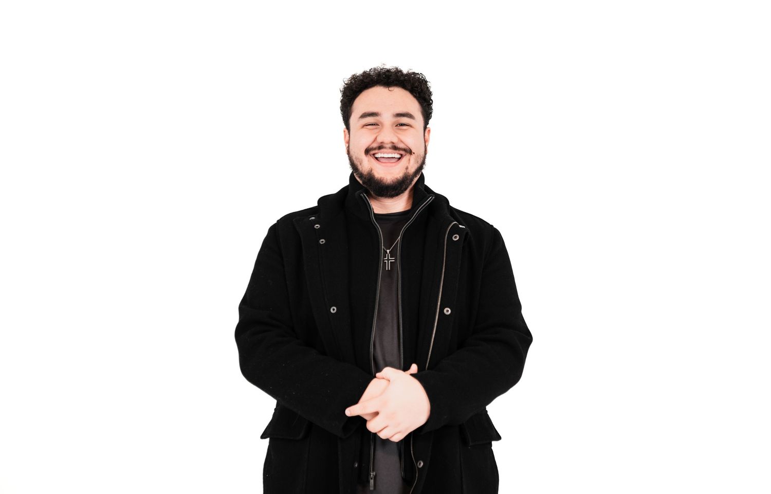 A person wearing a black winter coat smiles warmly while standing against a white background.