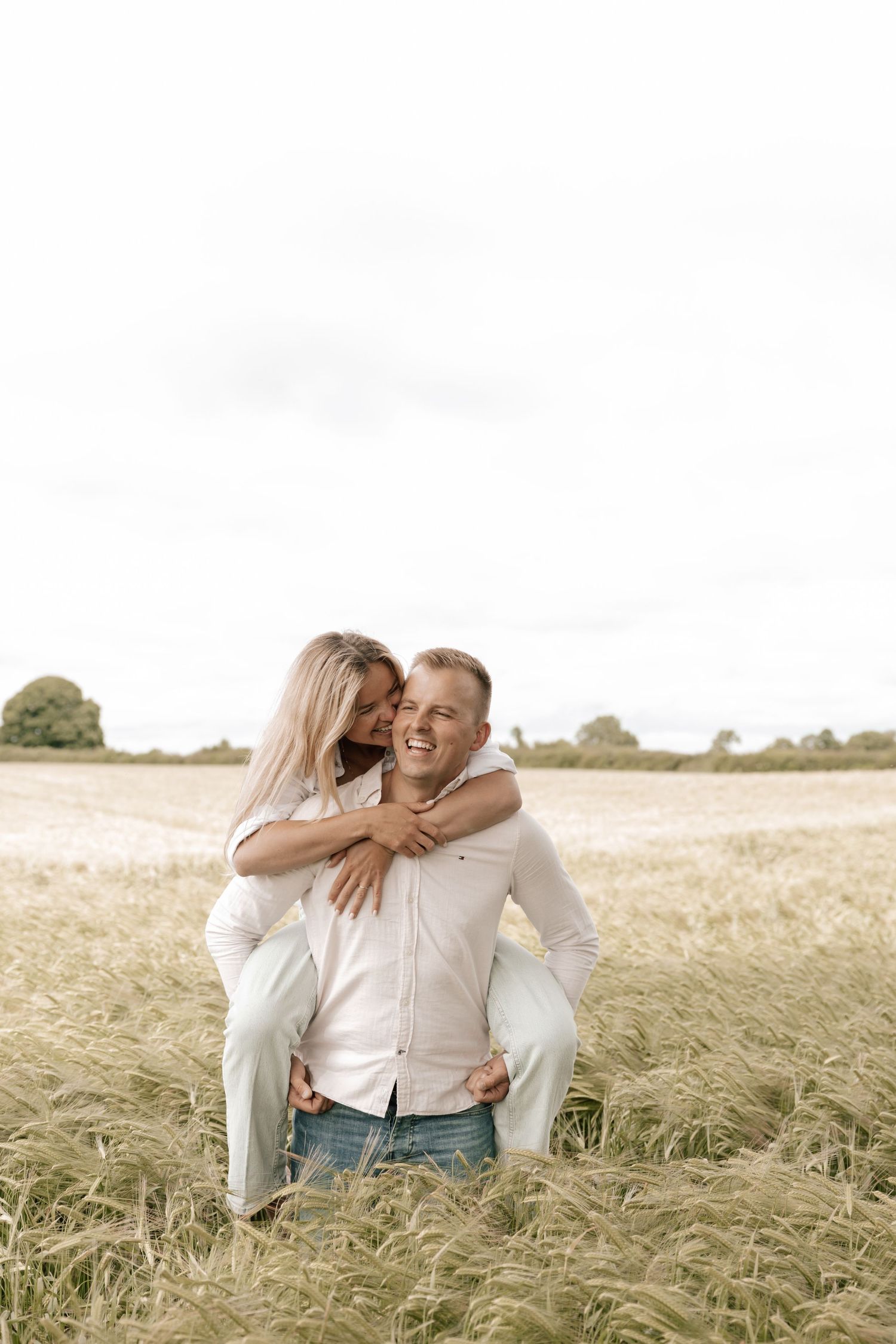 A couple shares an intimate moment while enjoying a piggyback ride in a golden wheat field at sunset.