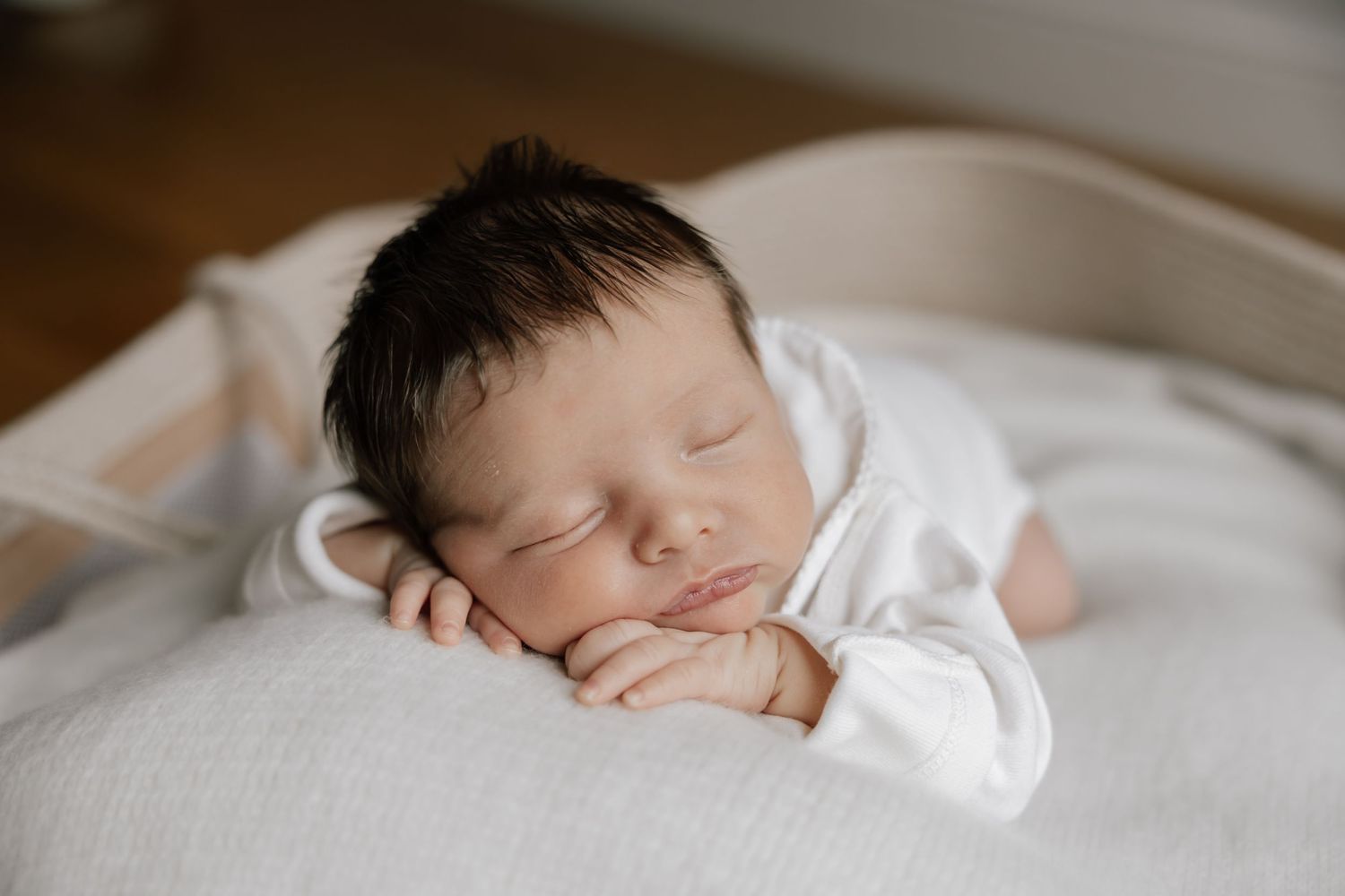 Peaceful sleeping newborn baby wearing white clothes rests on soft white bedding.