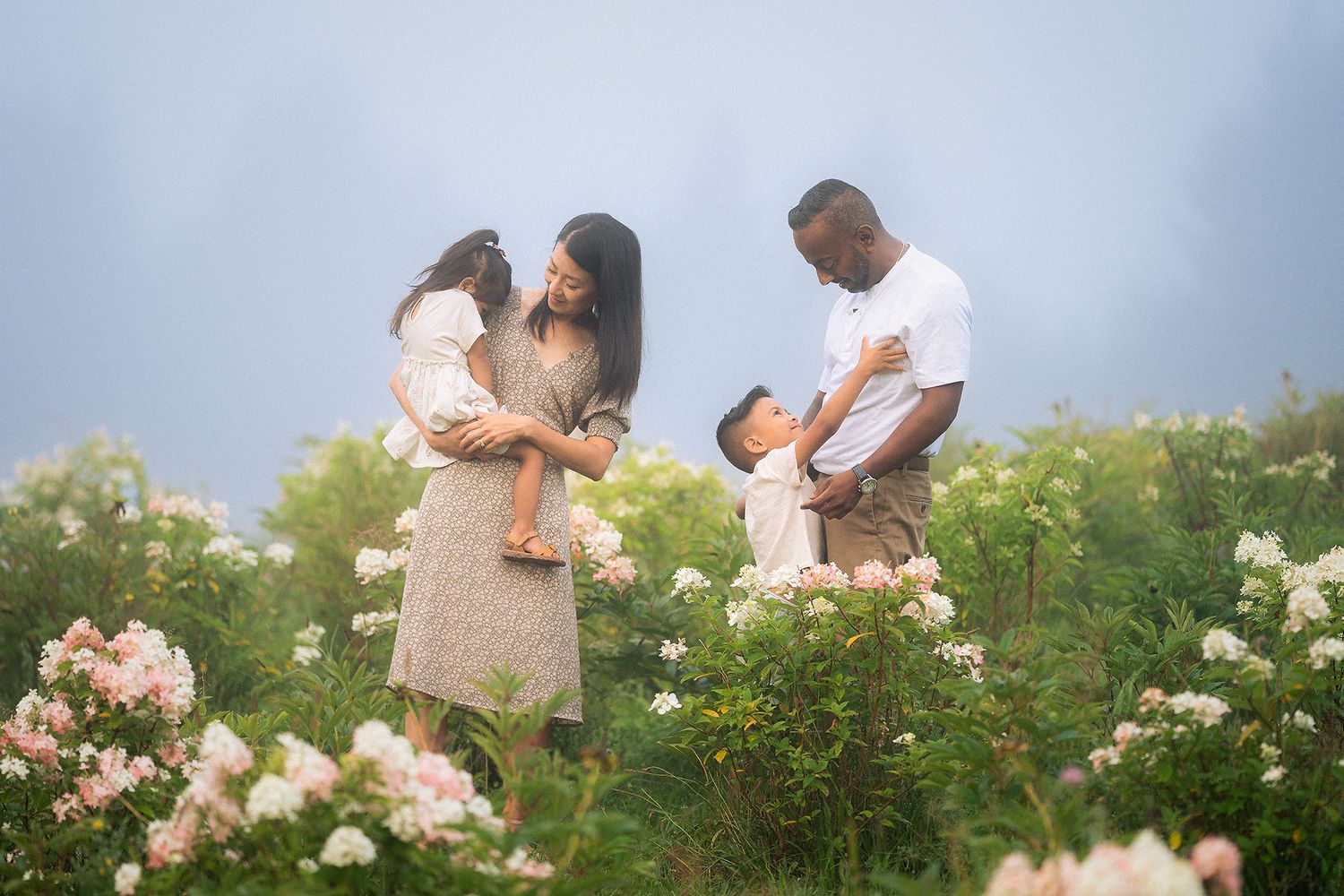 A couple shares a romantic moment together in a blooming flower garden on a misty summer day.
