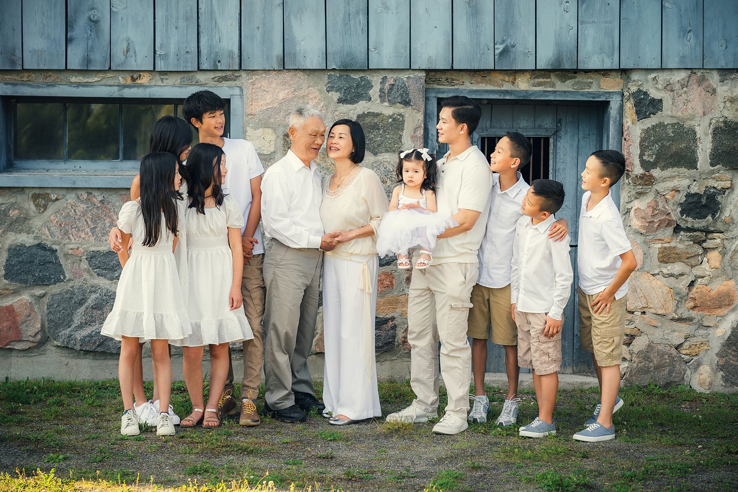 A panoramic collage of a wedding party wearing white and beige outfits posing against a rustic stone wall.