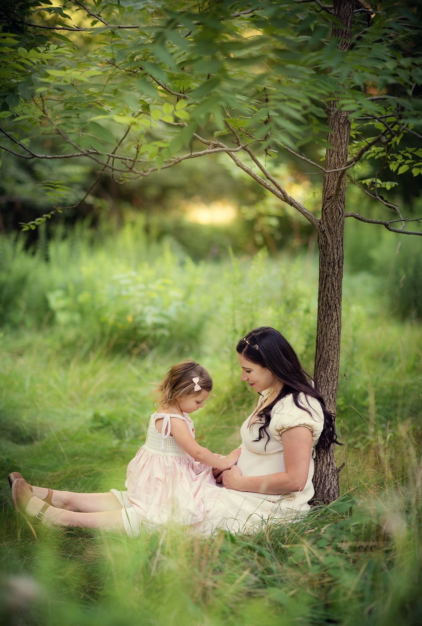 A dreamy outdoor scene in a lush green garden shows a tender moment between parent and child under a tree.