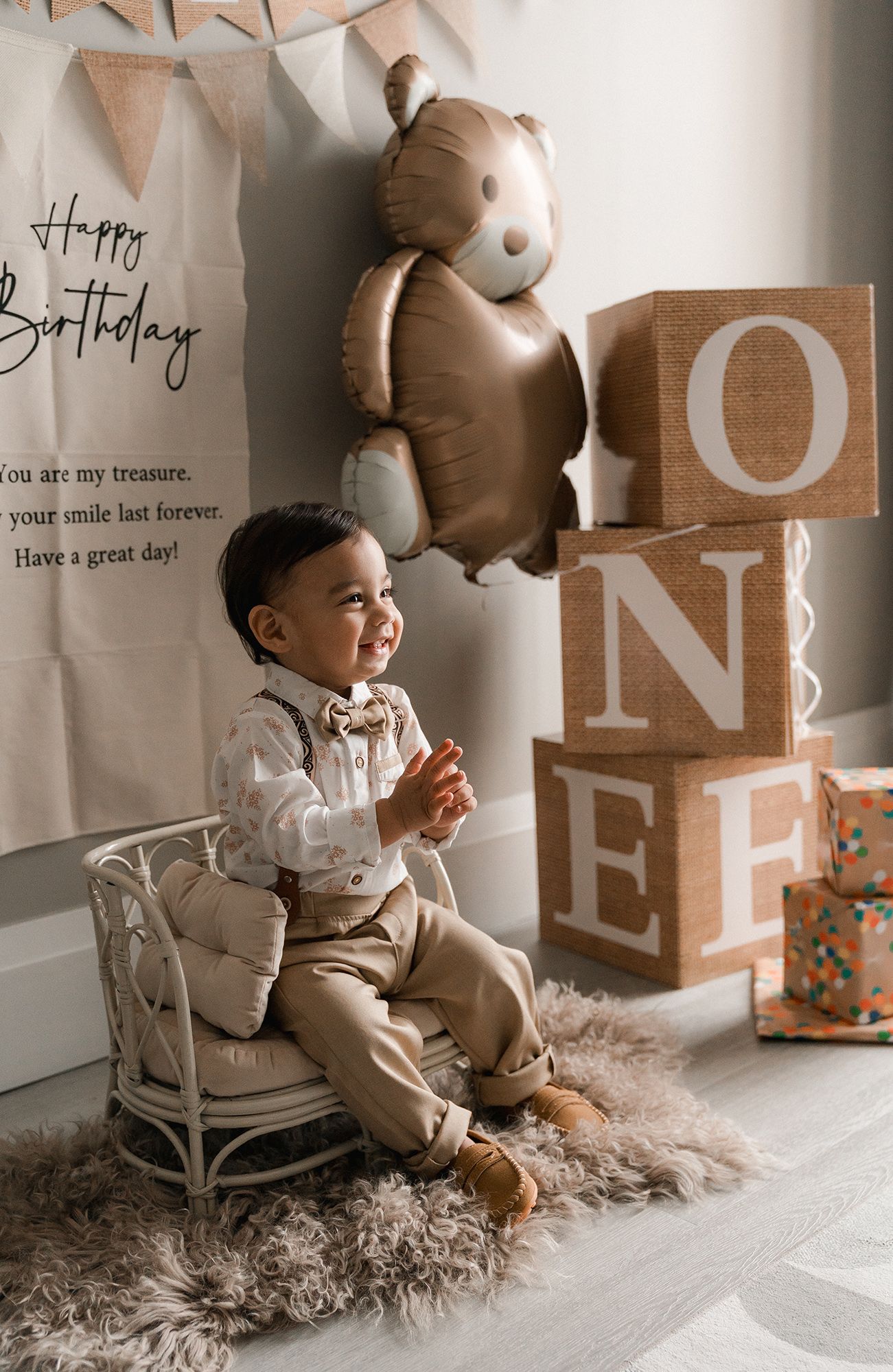 First birthday celebration setup with large ONE blocks, teddy bear balloon and child sitting in white vintage chair.