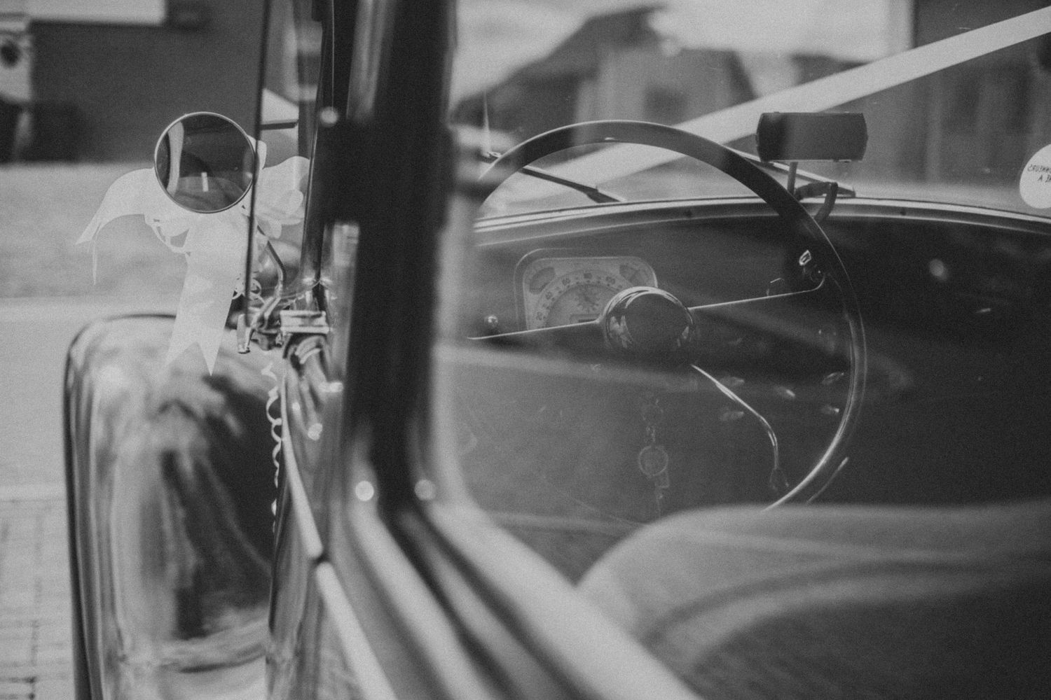 Black and white view through vintage car window showing side mirror and dashboard details.