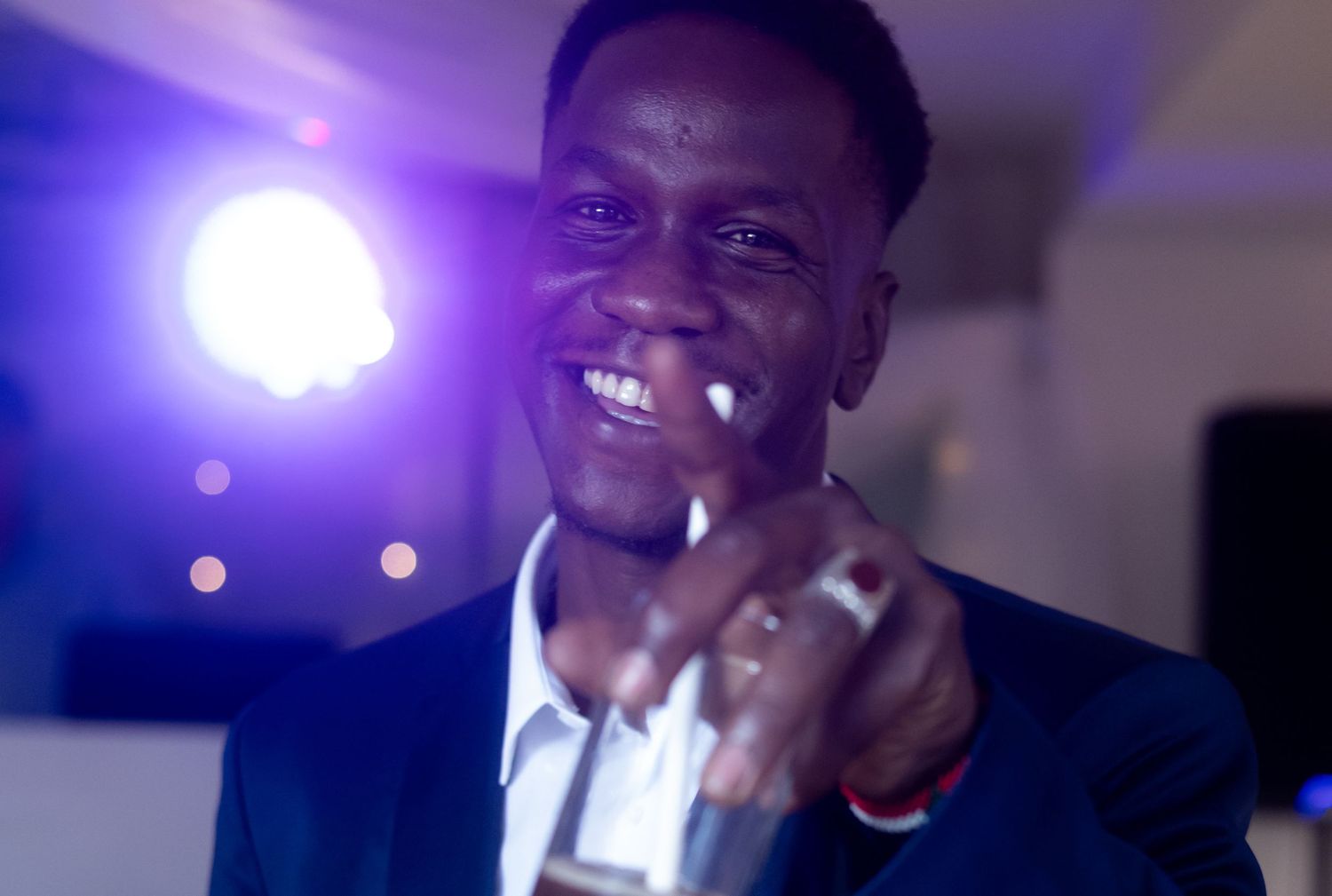Entertainment performer smiling brightly while speaking into microphone with purple stage lighting in background.