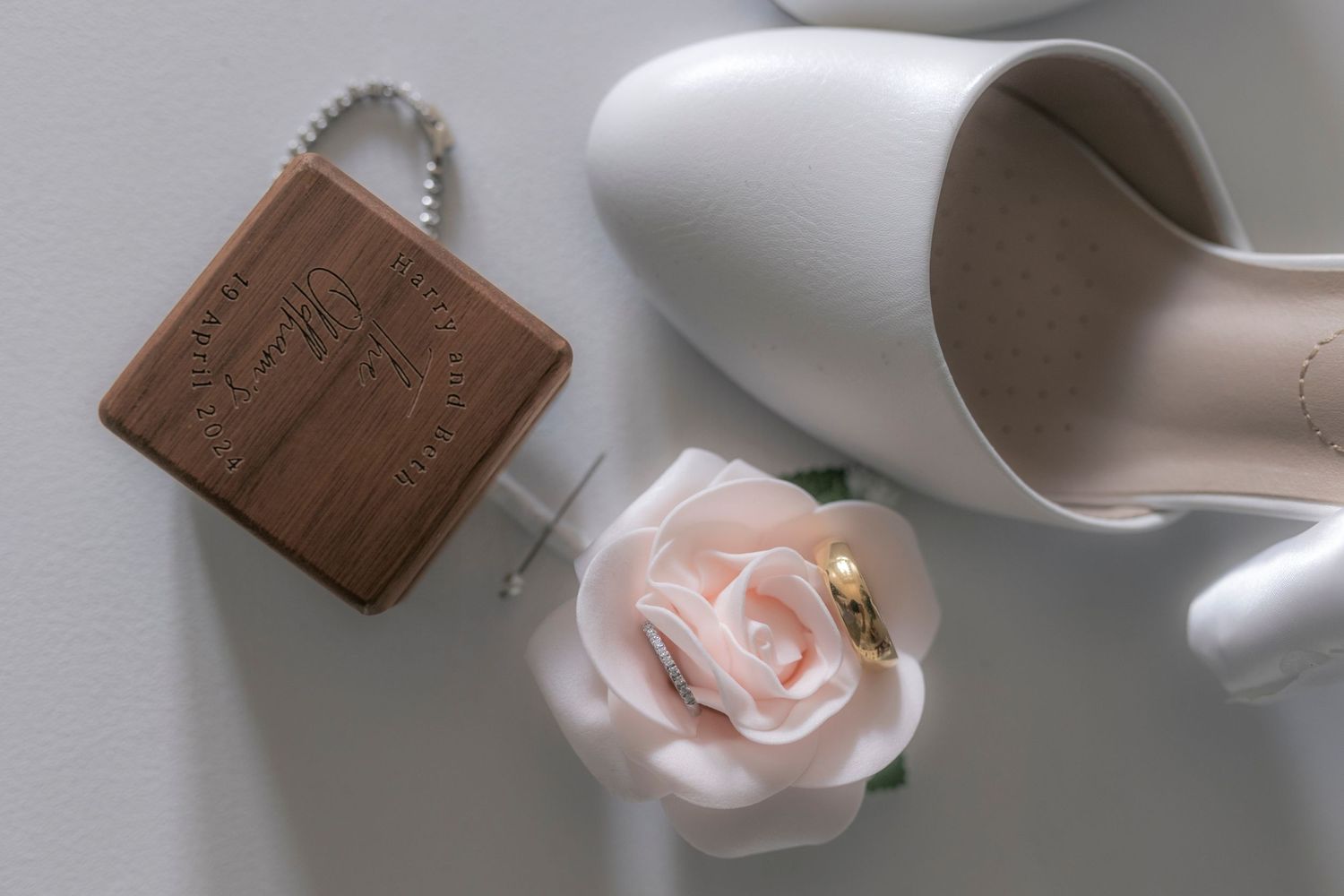 Wedding details featuring a brown leather item, white shoe, and delicate pink rose on a light background.