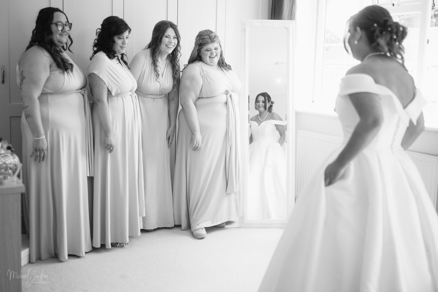 Classic black and white photo of a bridal party watching the bride in her wedding dress.