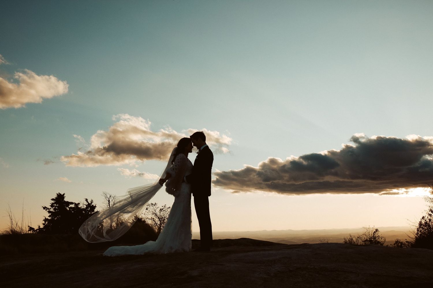 A romantic silhouette of two people kissing against a dramatic sunset sky with clouds in the background.