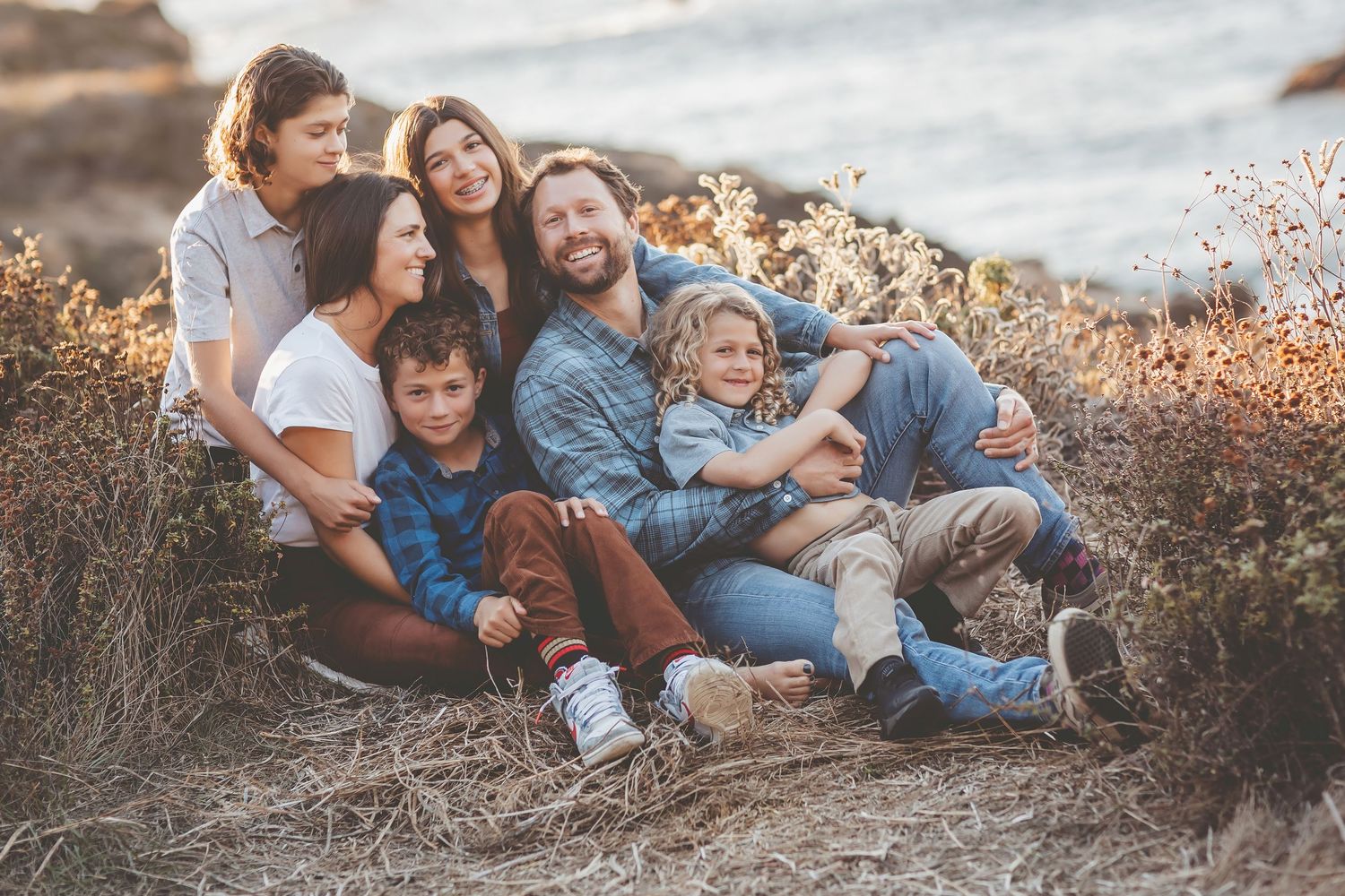 Family enjoying warm sunset light together while laying on ground in casual denim outfits during outdoor photo session.