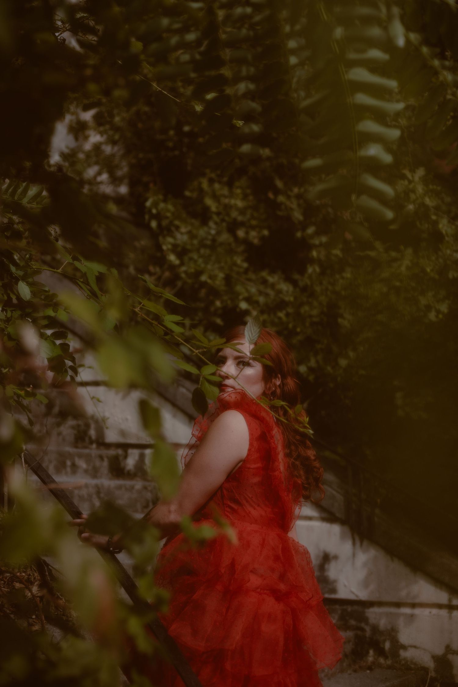 Moody portrait of client wearing a red dress while walking up the stairs of an abandoned asylum in British Columbia.