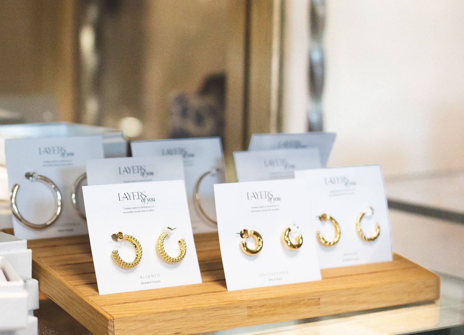 Gold and silver hoop earrings displayed on white branded cards atop a wooden tray in a boutique jewelry store.