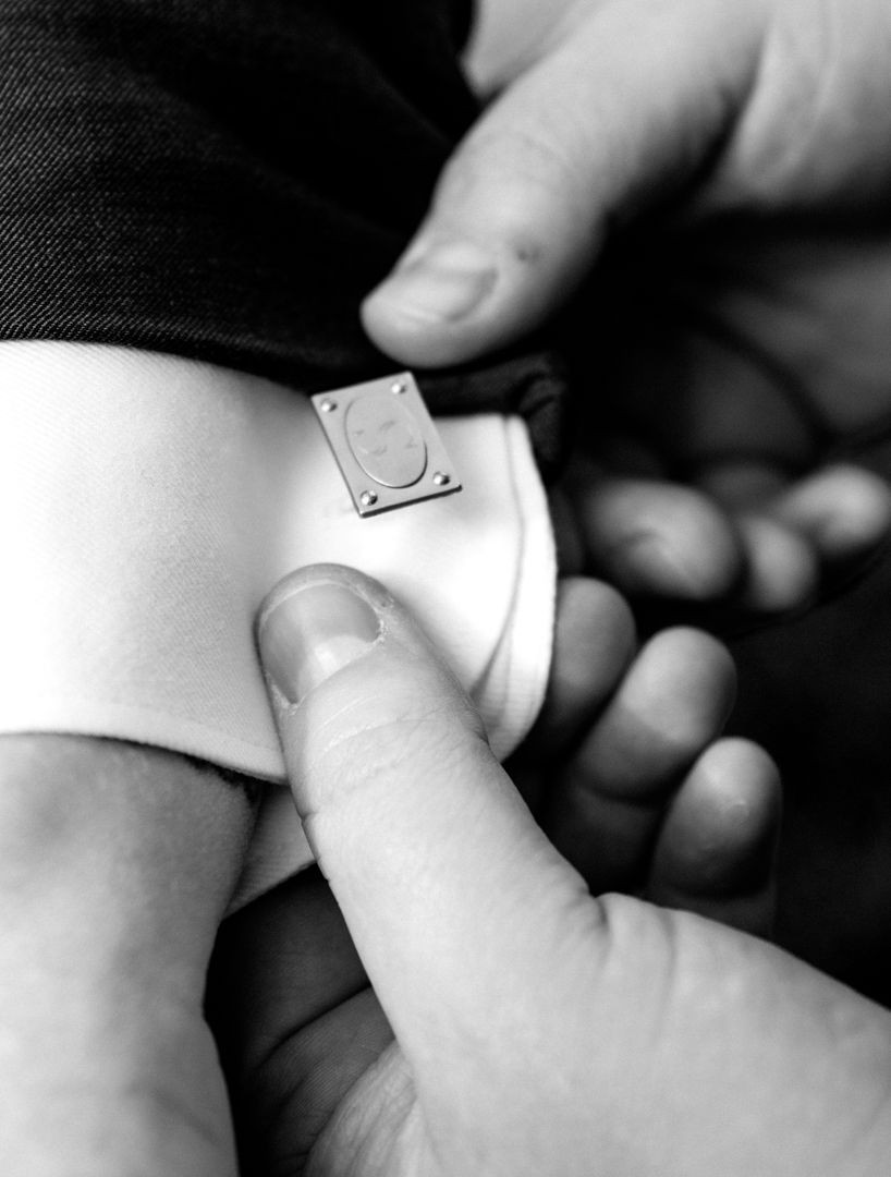 Black and white close-up of hands adjusting a small metal cufflink on a white dress shirt cuff beneath a dark suit sleeve.