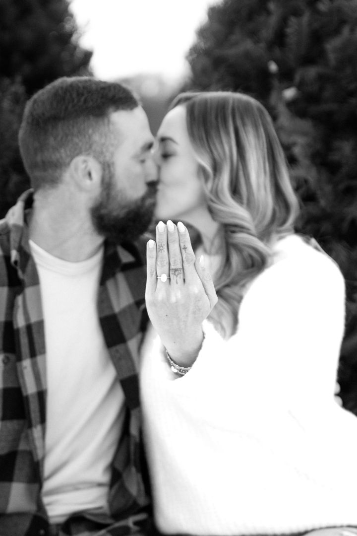 Black and white photo of a couple kissing as the woman holds up her hand to show off her sparkling engagement ring.