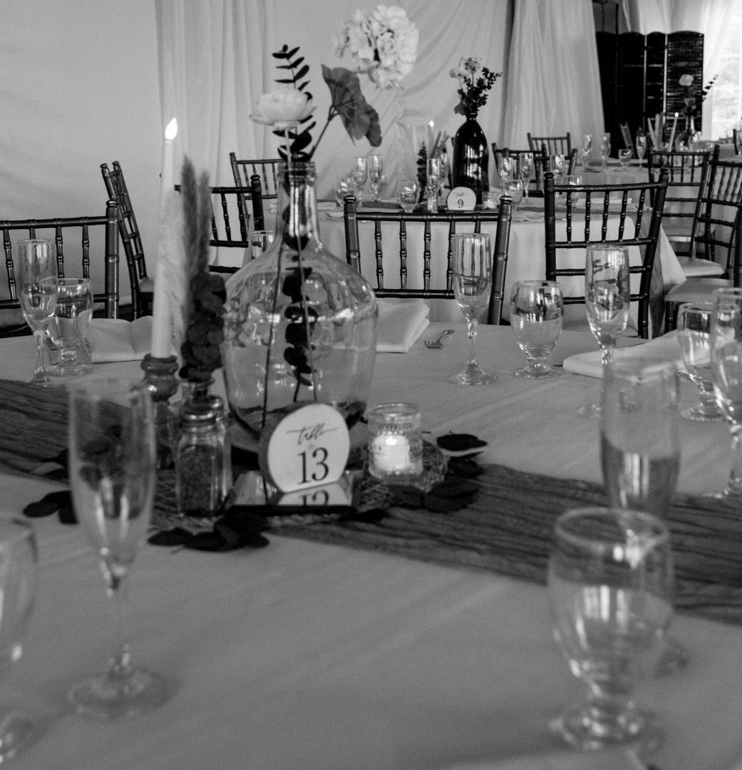 Black and white wedding reception table with a numbered 13 sign, candle, floral centerpiece, wine glasses and chiavari chairs.
