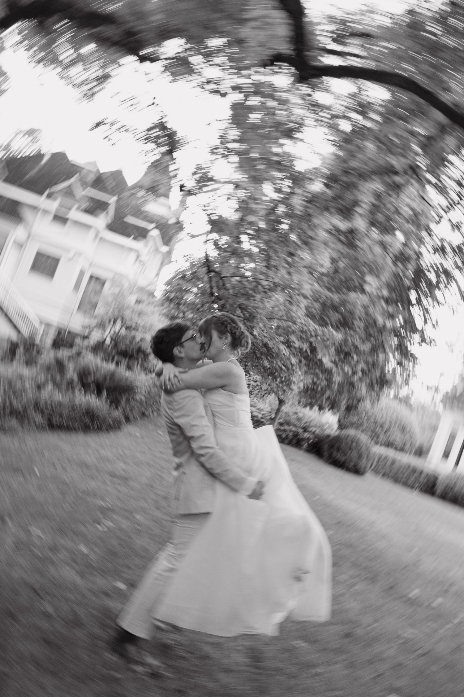 Black and white photo of bride and groom kissing outdoors with artistic spin blur effect.
