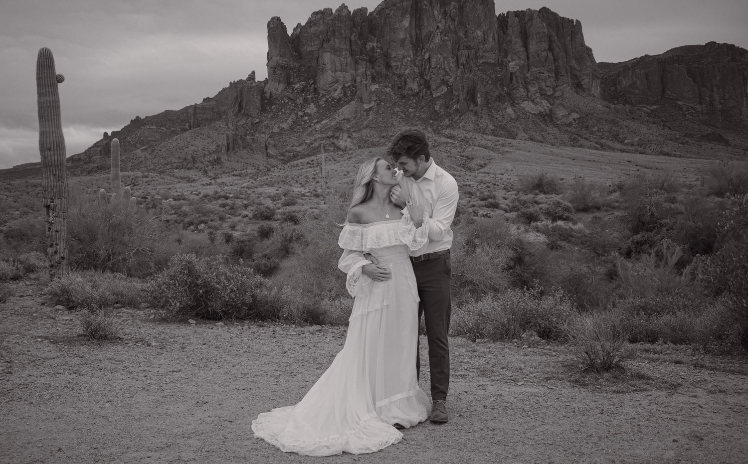 Black and white desert wedding photo of couple embracing near Superstition Mountains in Arizona.
