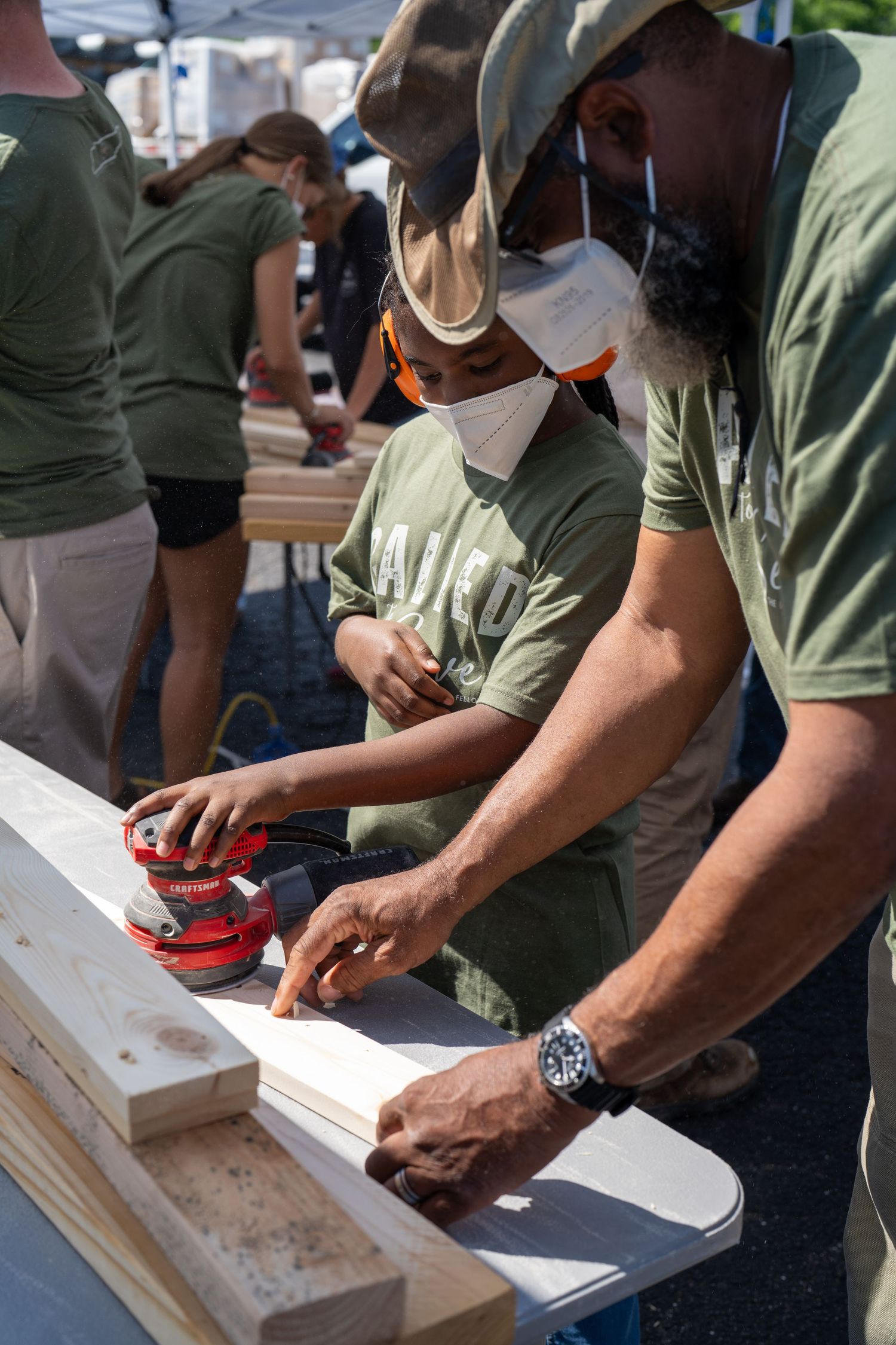 Volunteers from The Warehouse Fellowship sanding wooden boards together during an outdoor community service event.