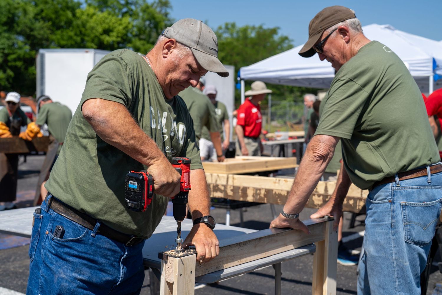 Volunteers from The Warehouse Fellowship drilling into wooden boards together during an outdoor community service event.