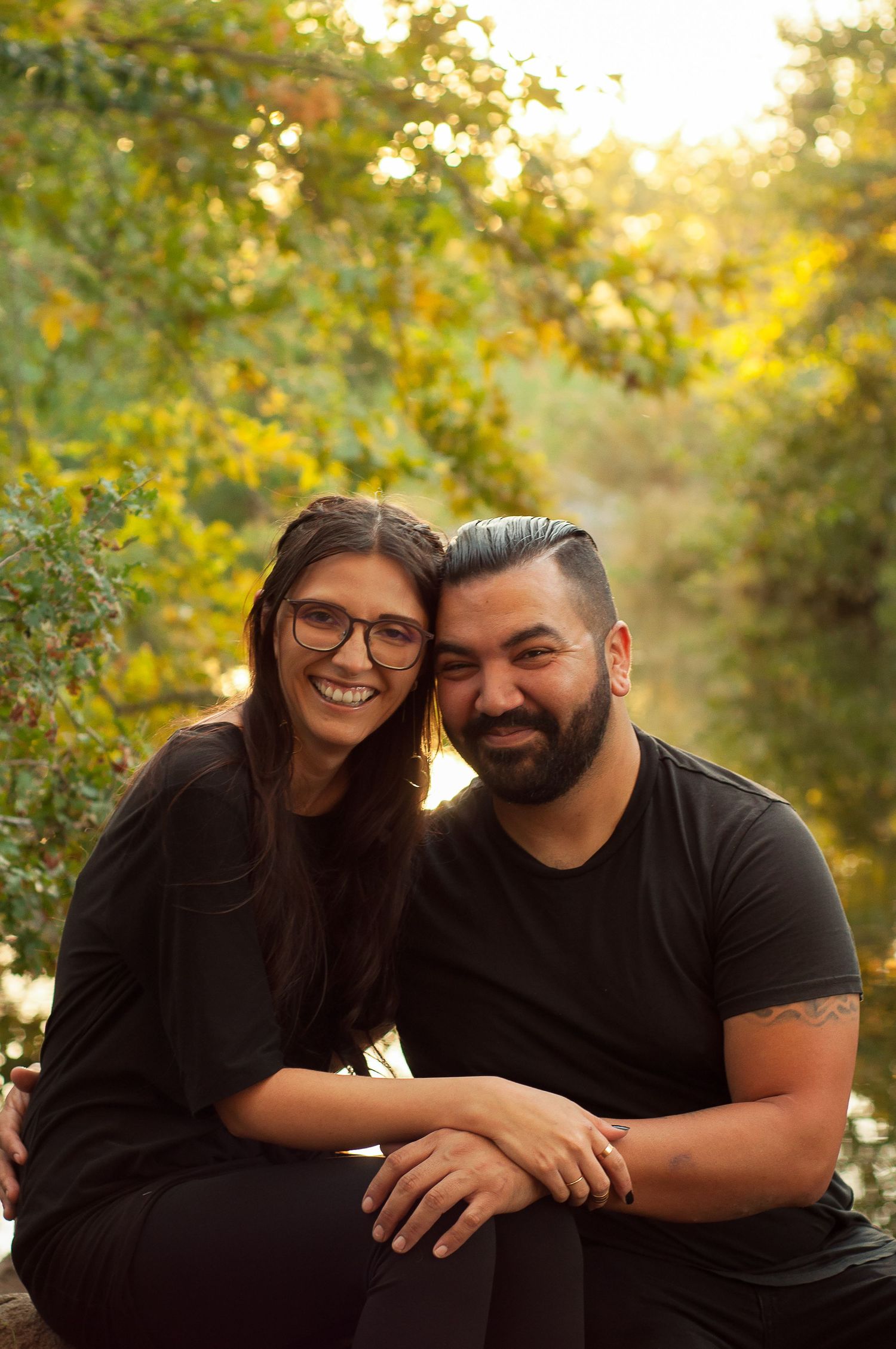 Couple smiling together beside a wooded creek during a fall portrait session.