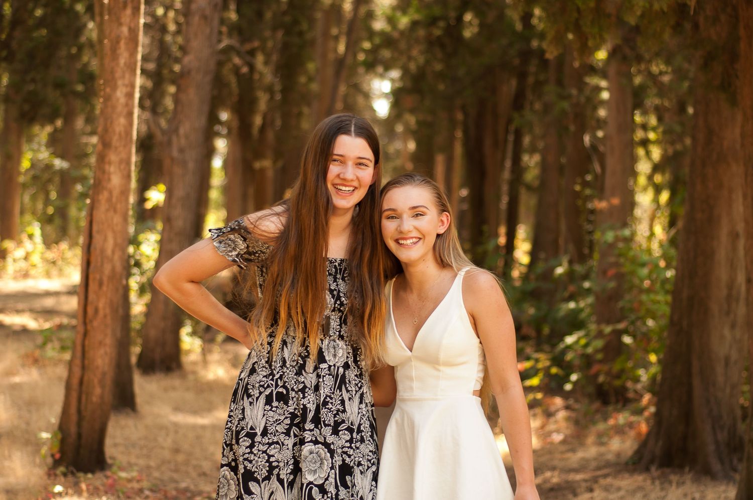 Two teenage girls smiling together during a warm outdoor family portrait session.