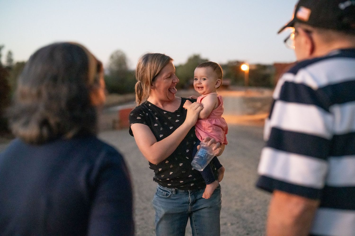 Woman holding a young child while talking with family at an outdoor gathering.