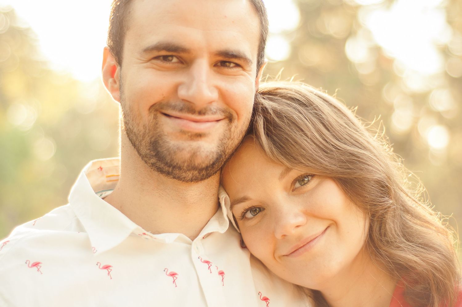Close-up portrait of a couple smiling and leaning together in warm evening light.