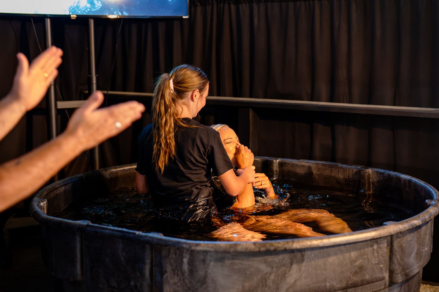 A young woman baptizing her aunt during a church service.