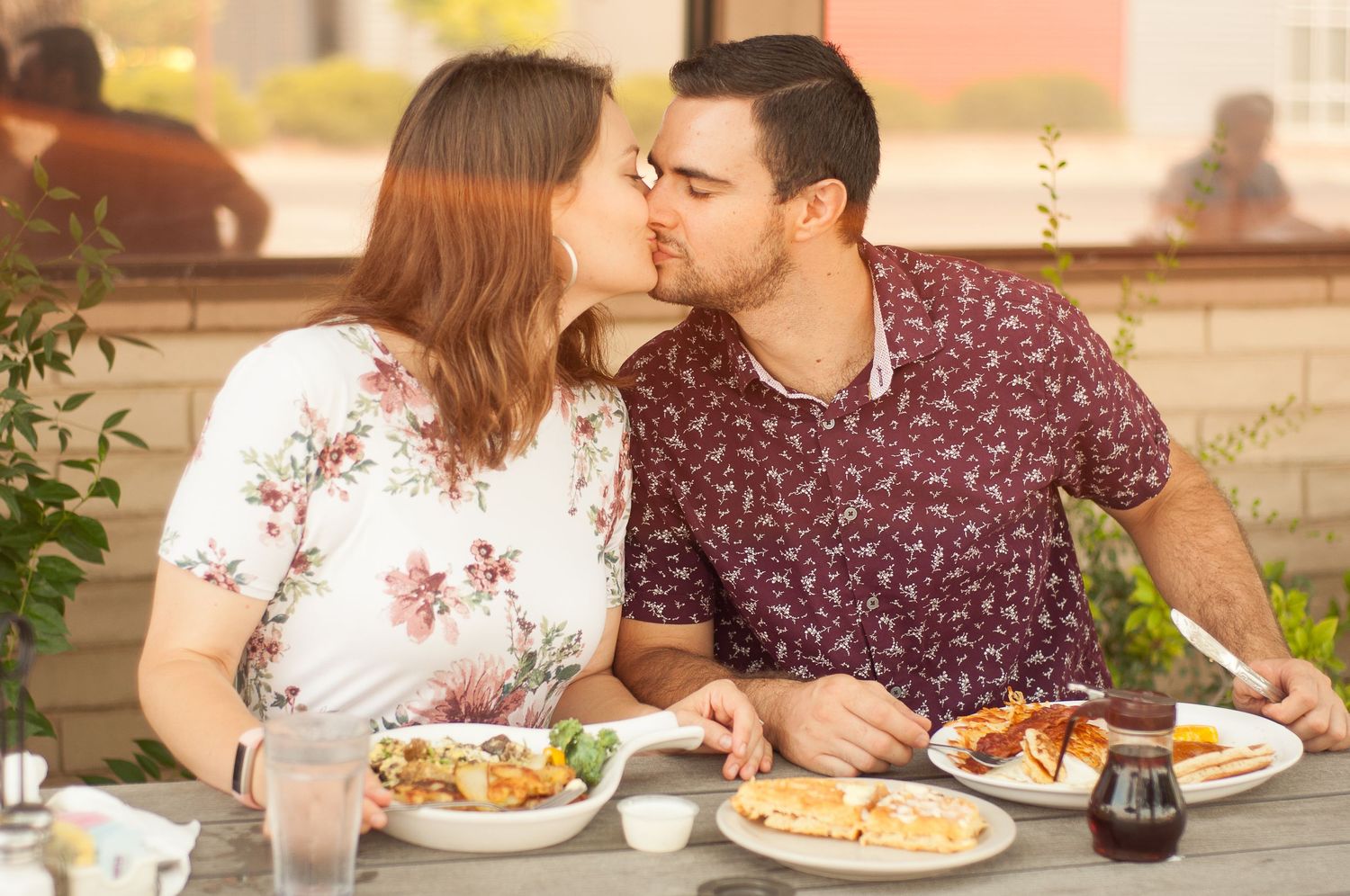 Couple sharing a kiss in the warm sunlight while dining together at an outdoor brunch restaurant.