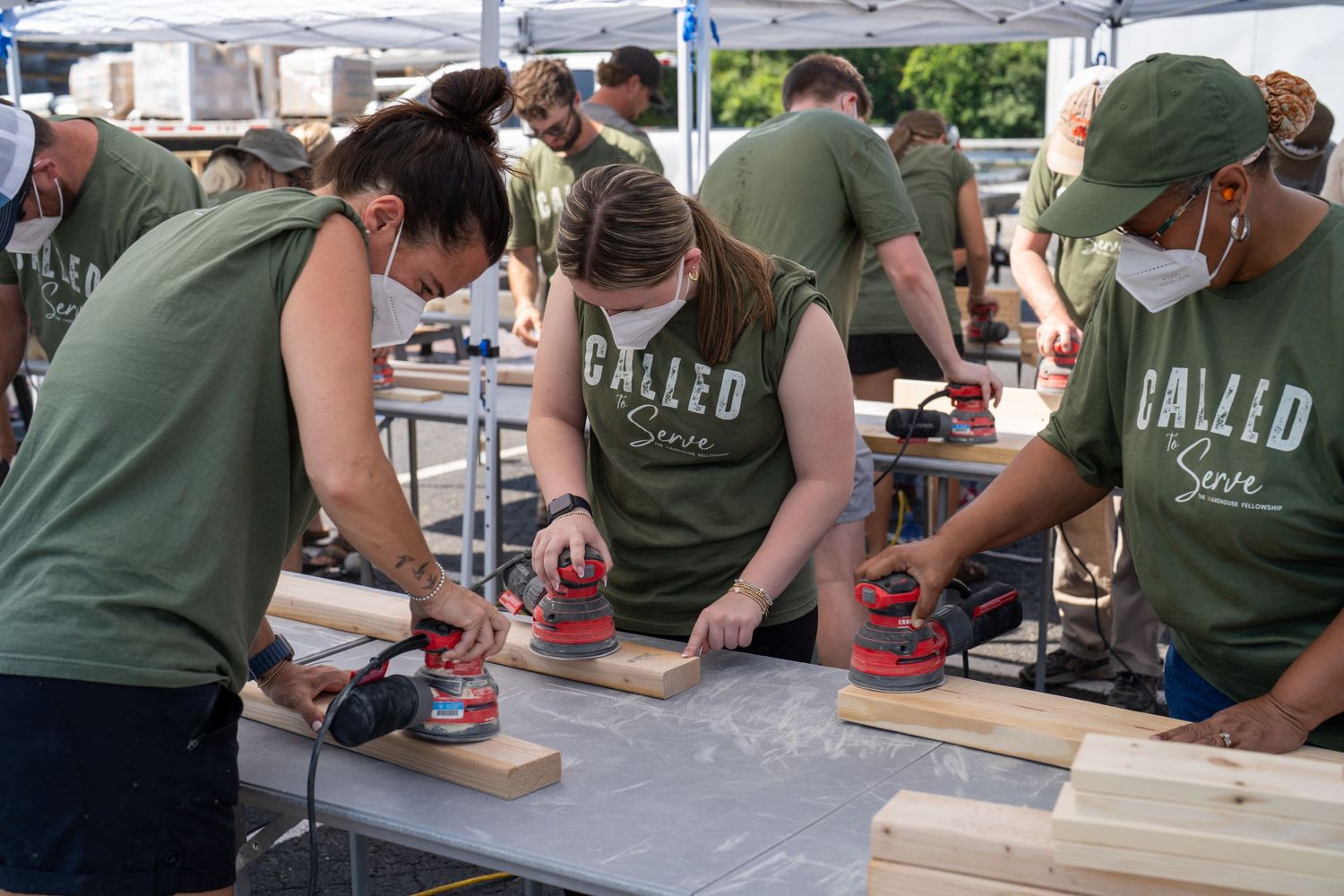 Volunteers from The Warehouse Fellowship sanding wooden boards together during an outdoor community service event.