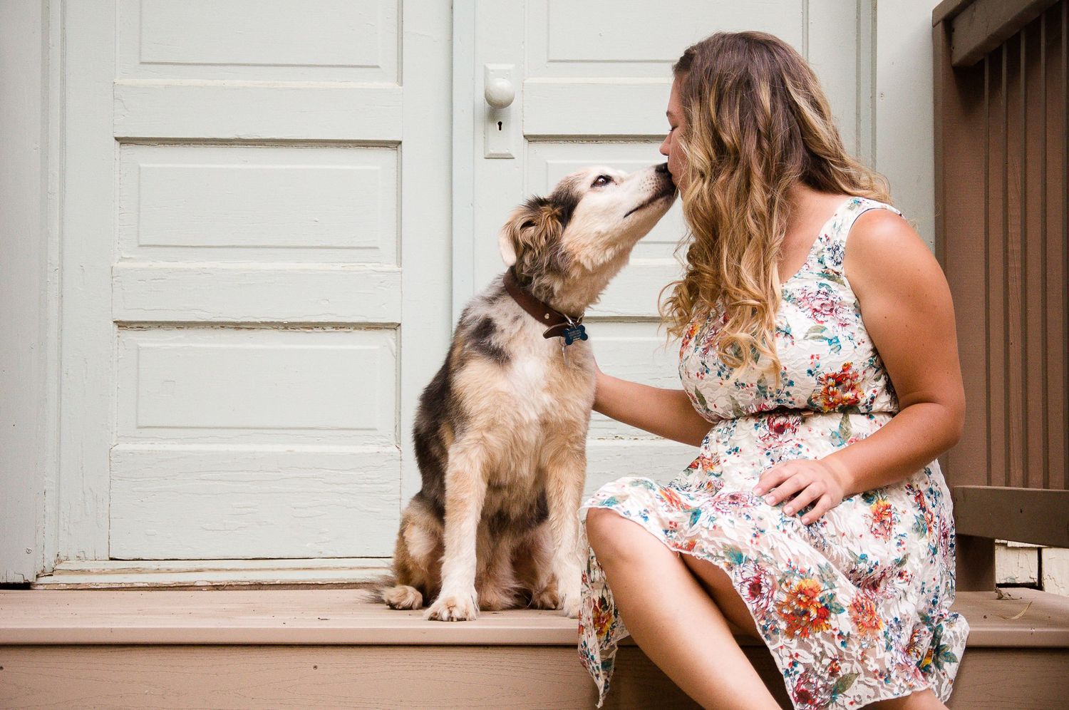Woman sharing an affectionate moment with her dog on a sunny front porch.