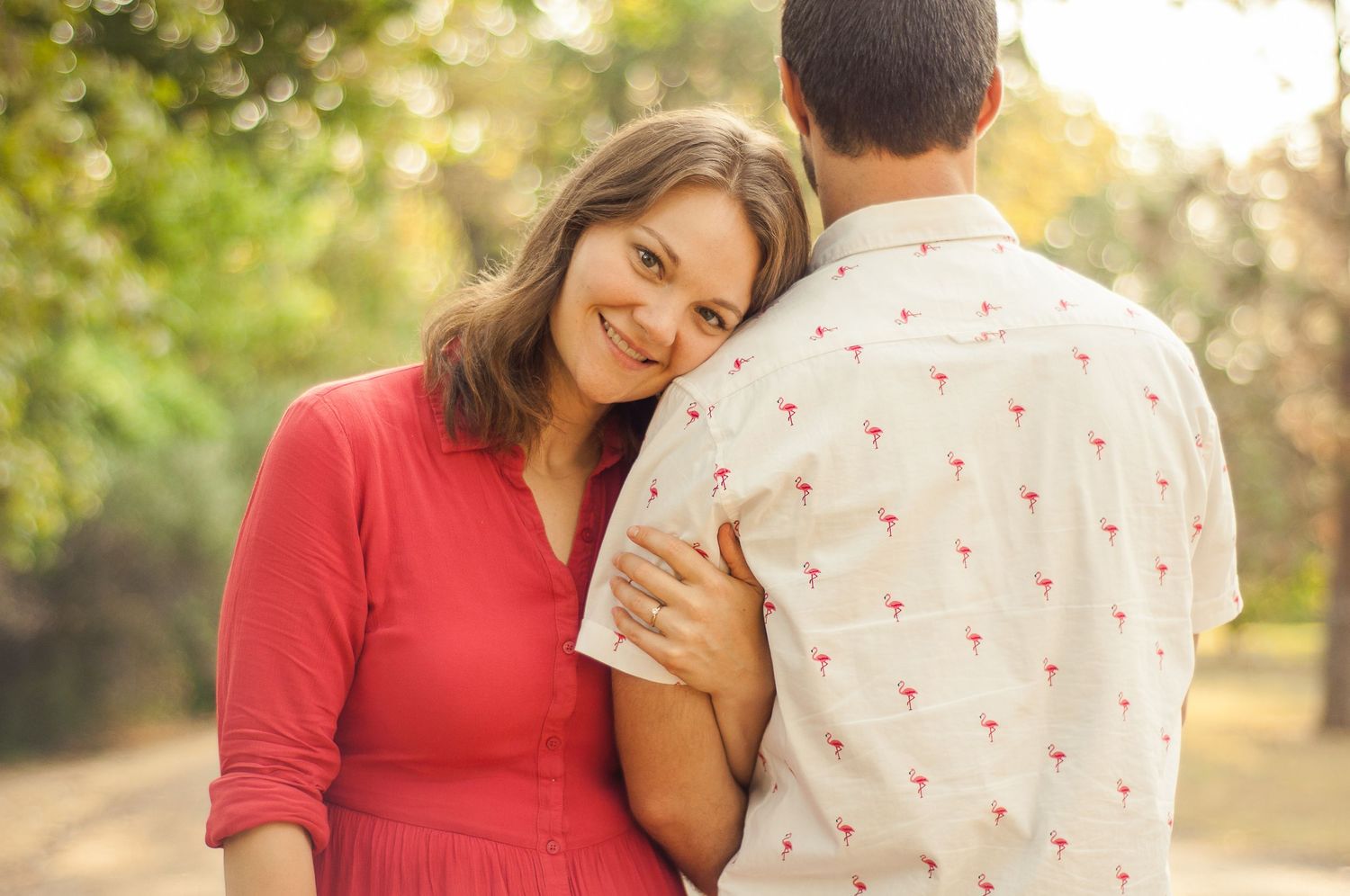 Woman resting her head on her partner's shoulder during a warm outdoor couples session.