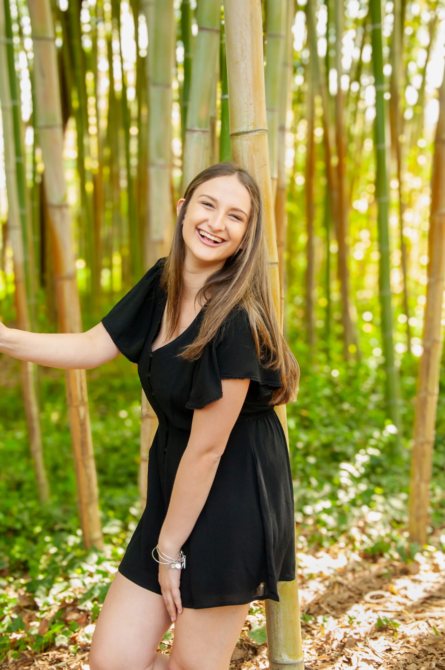 Young woman smiling among tall bamboo shoots during an outdoor portrait session.