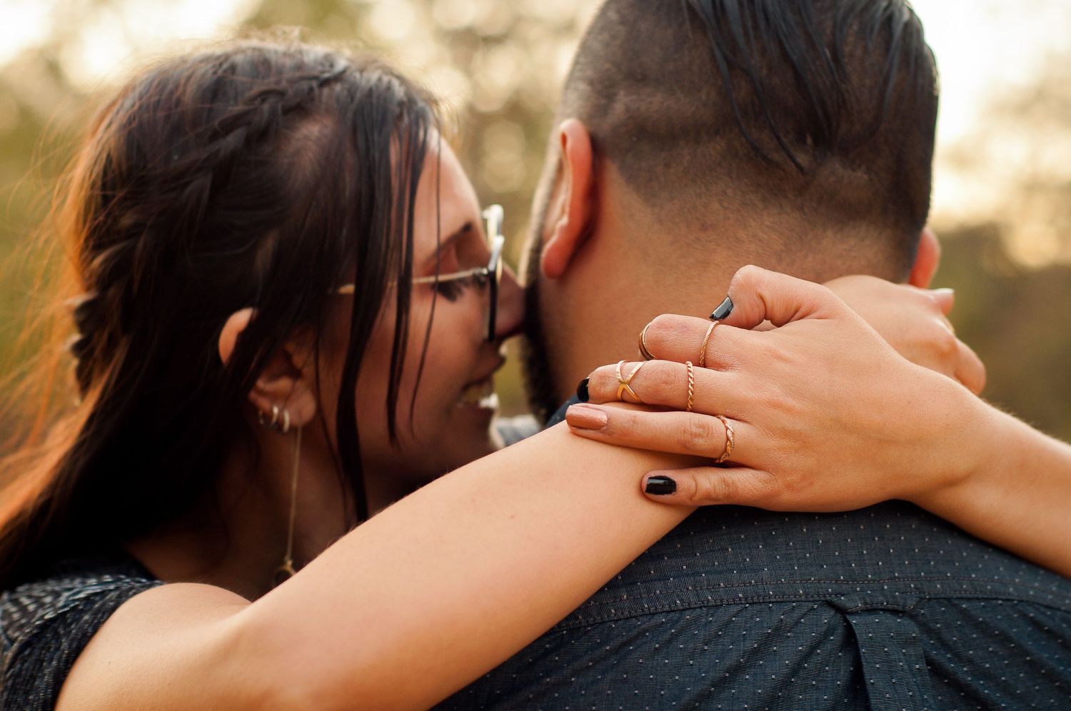 Couple embracing during a warm outdoor portrait session and showing off engagement ring.