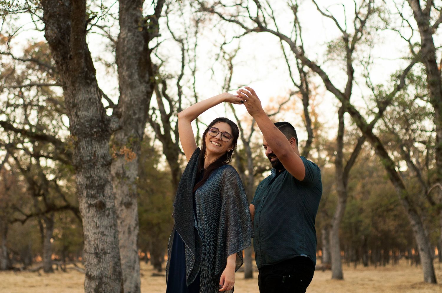 Couple playfully twirling together beneath the trees during an outdoor portrait session.