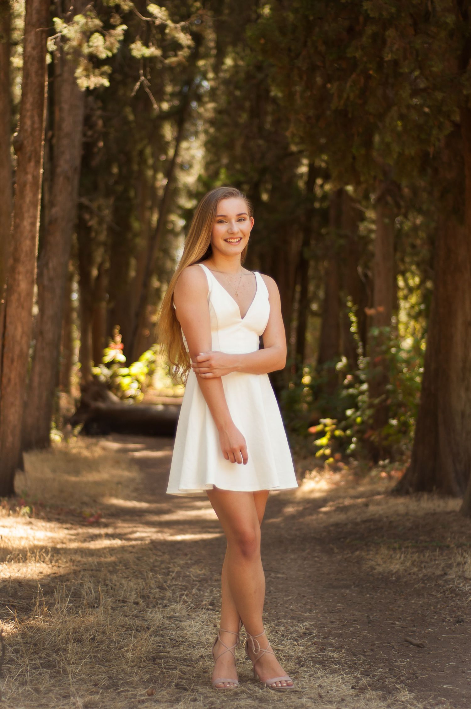 Young woman posing among tall trees during an outdoor portrait session.