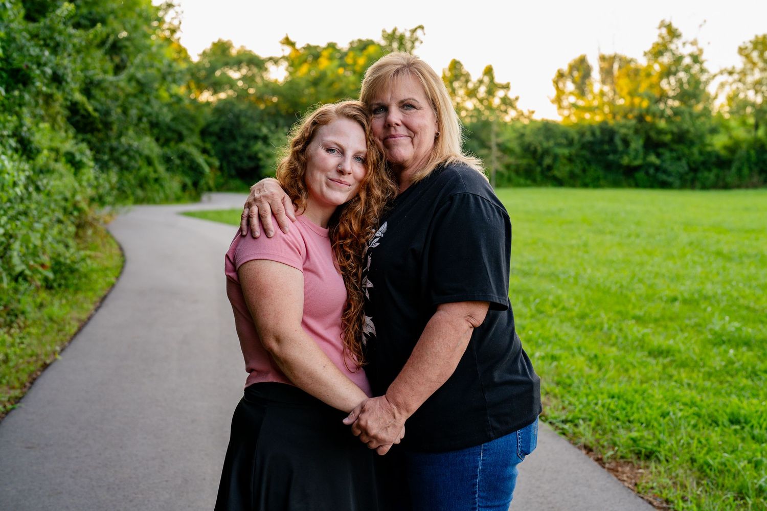 A mother and daughter standing together on a path during an outdoor portrait session at sunset.
