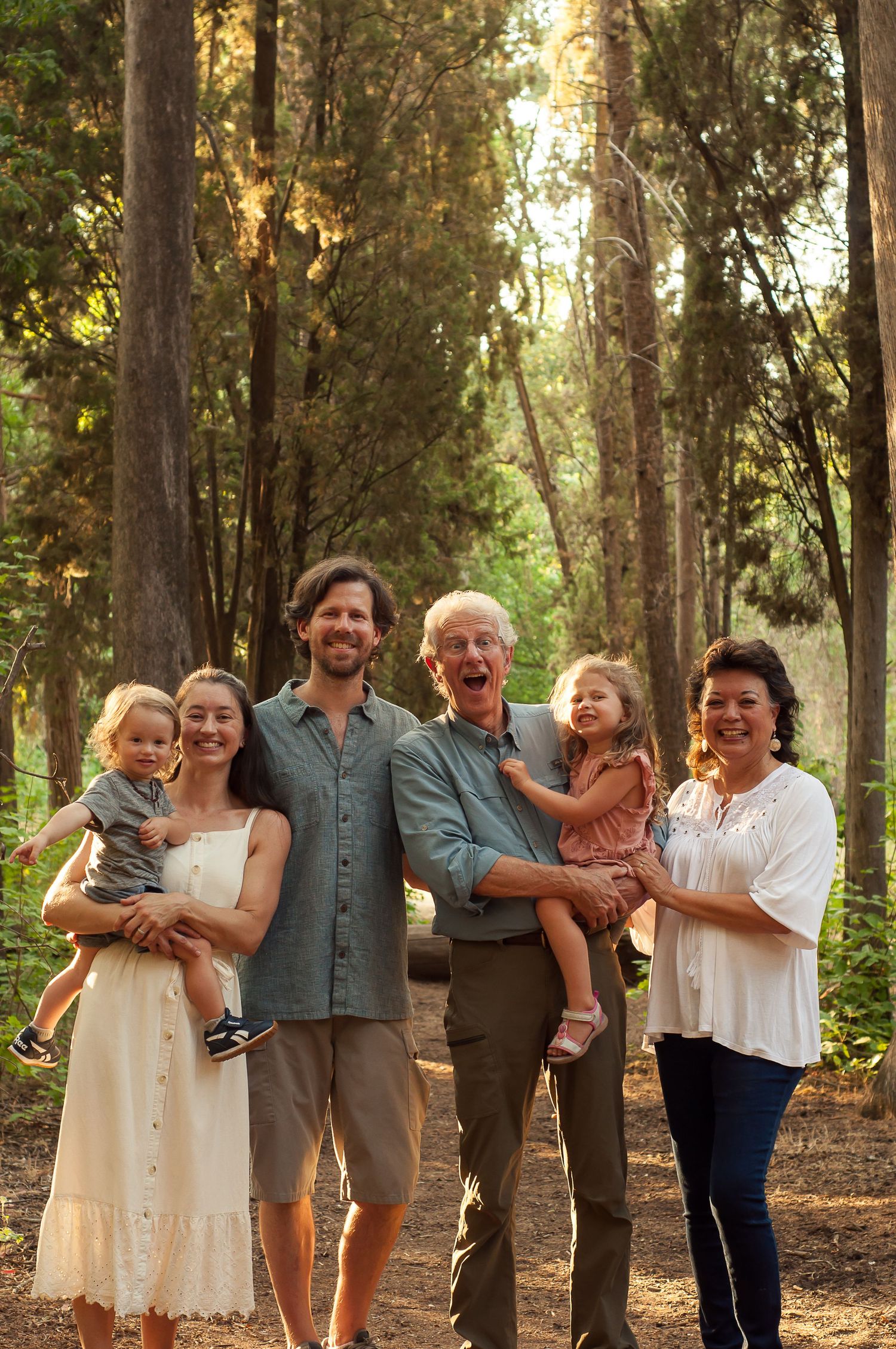 Multigenerational family standing together among tall trees during an outdoor portrait session.