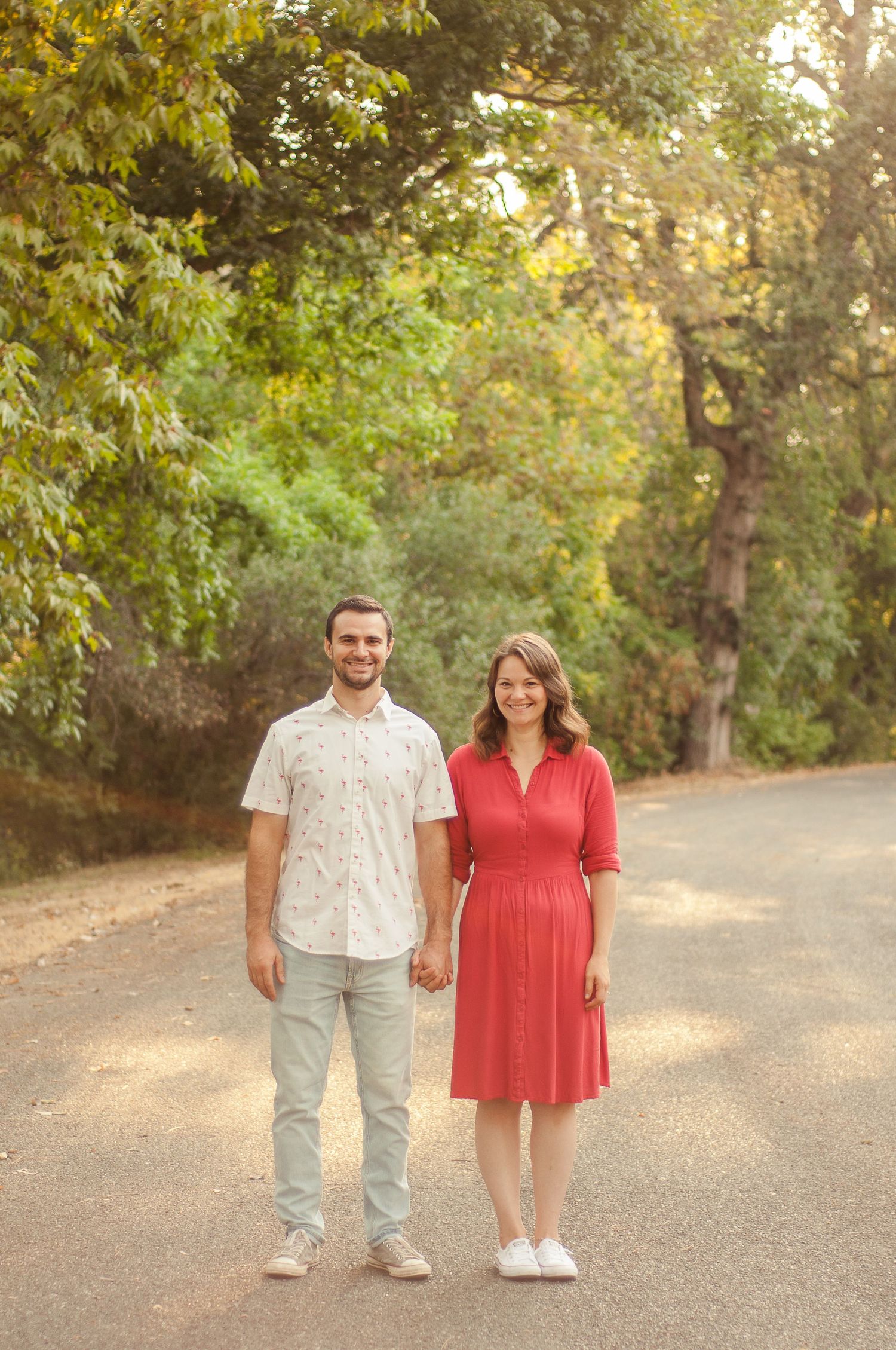 Couple standing together on a quiet tree-lined road during an outdoor portrait session.