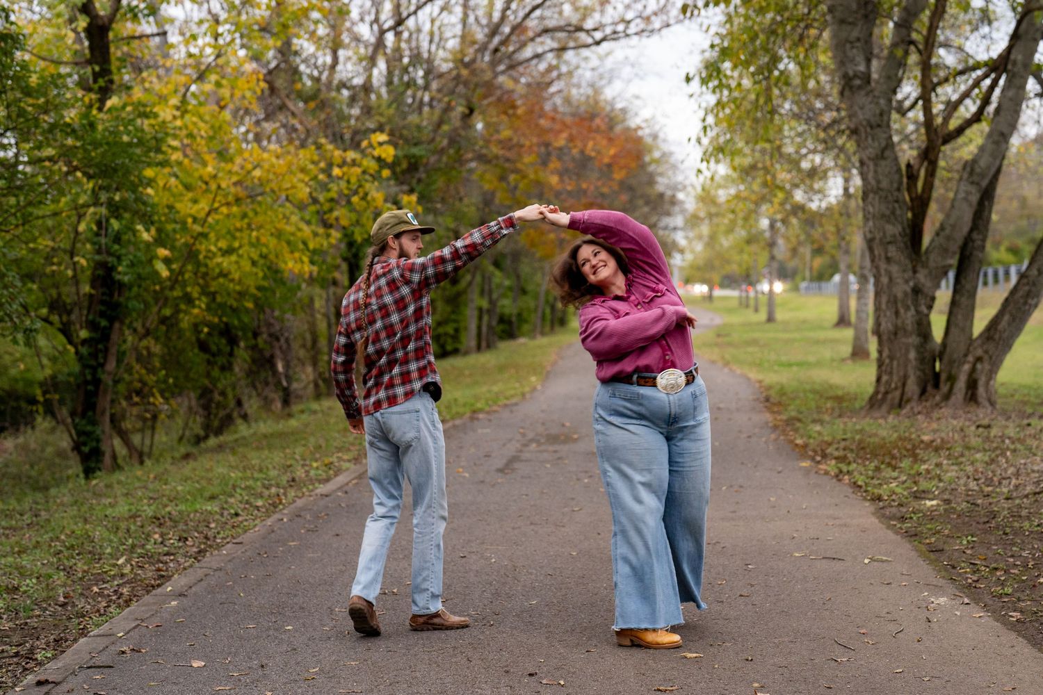 Couple dancing together on a tree-lined path during a fall portrait session.
