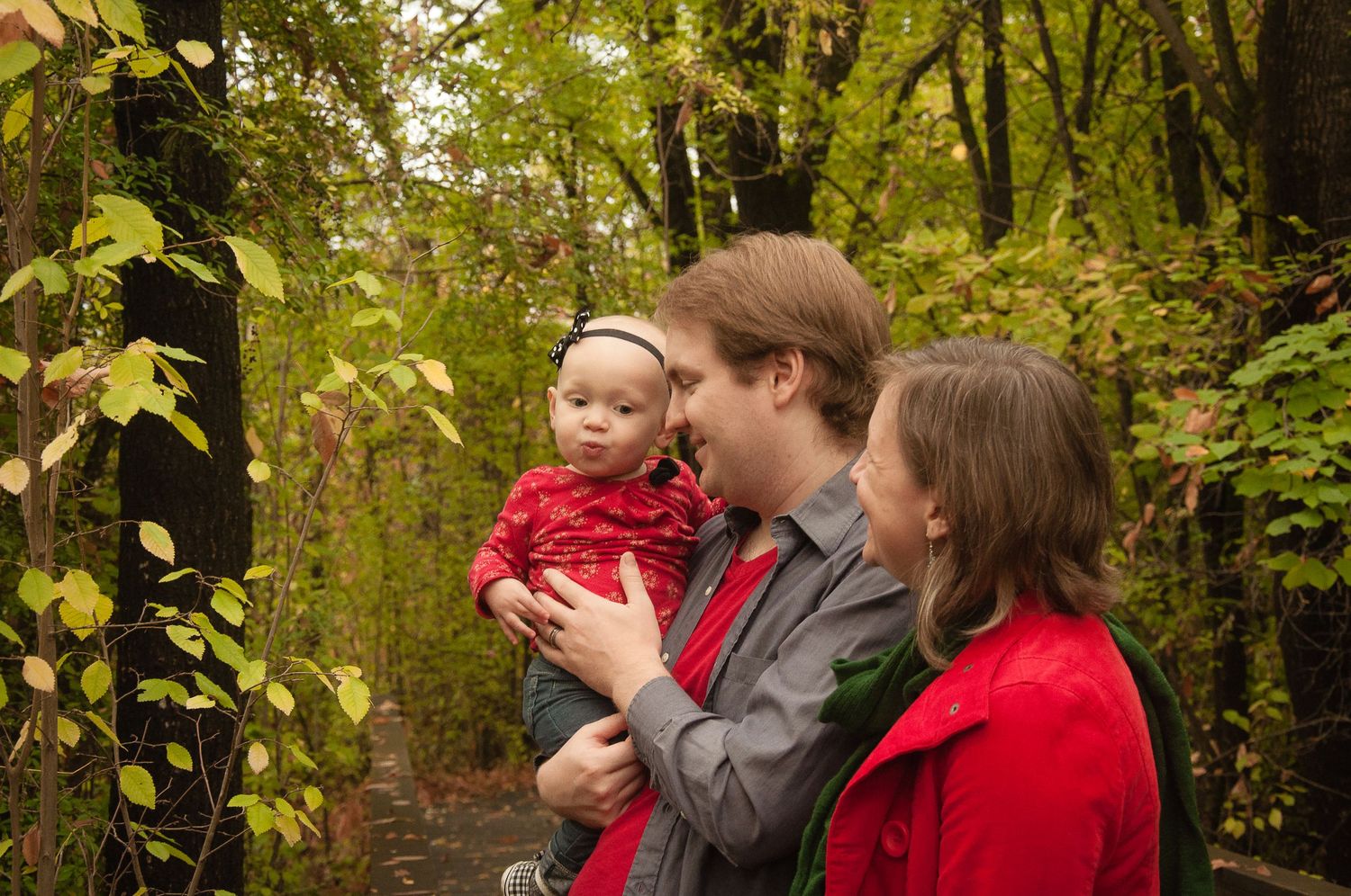 Parents holding their young child together during a wooded fall portrait session.