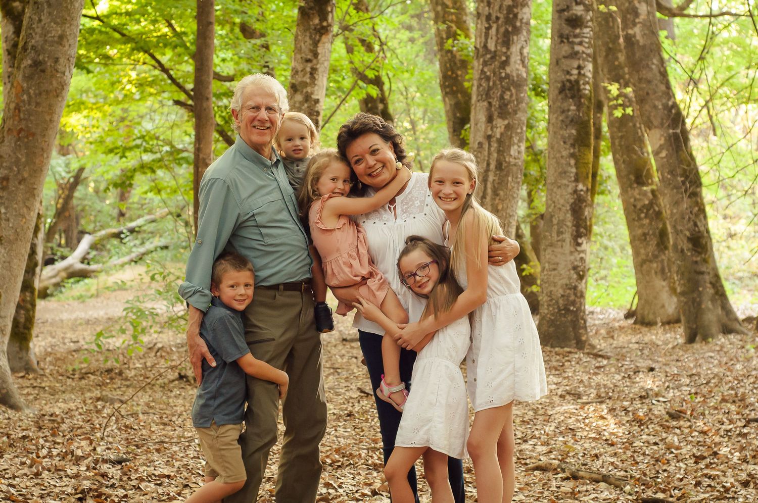 Grandparents and grandchildren gathered together among the trees for an outdoor portrait.