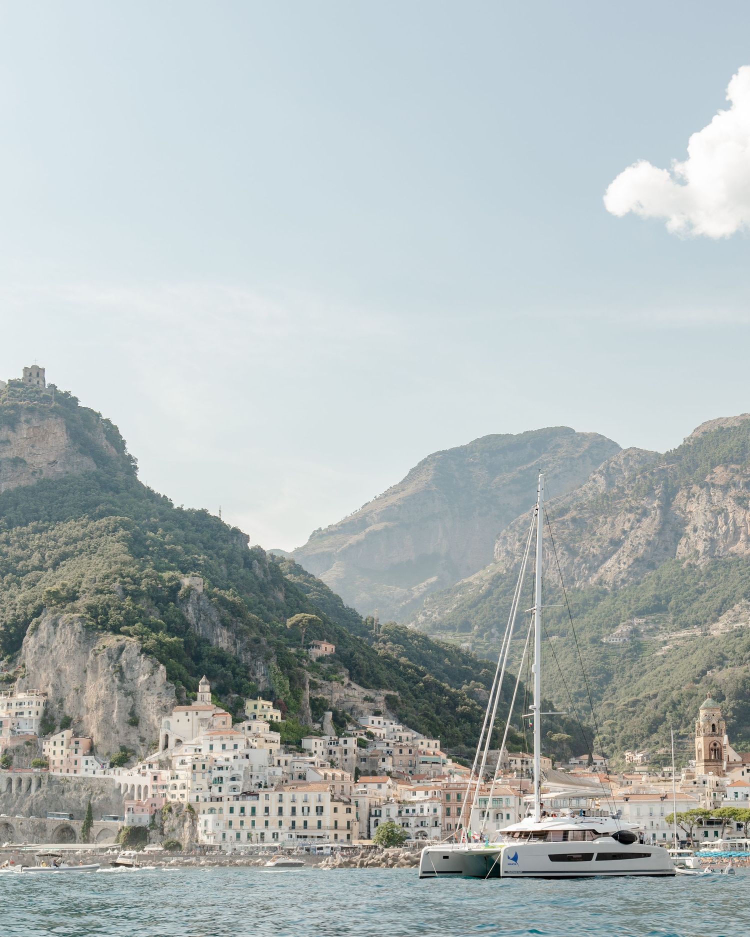 Amalfi Coast photographed from the ocean featuring a sailboat, mountains and buildings
