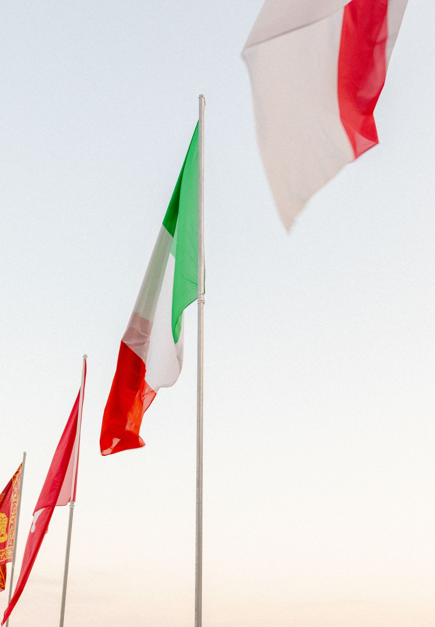 Three Italian flags in front of a blue sky flying in the wind