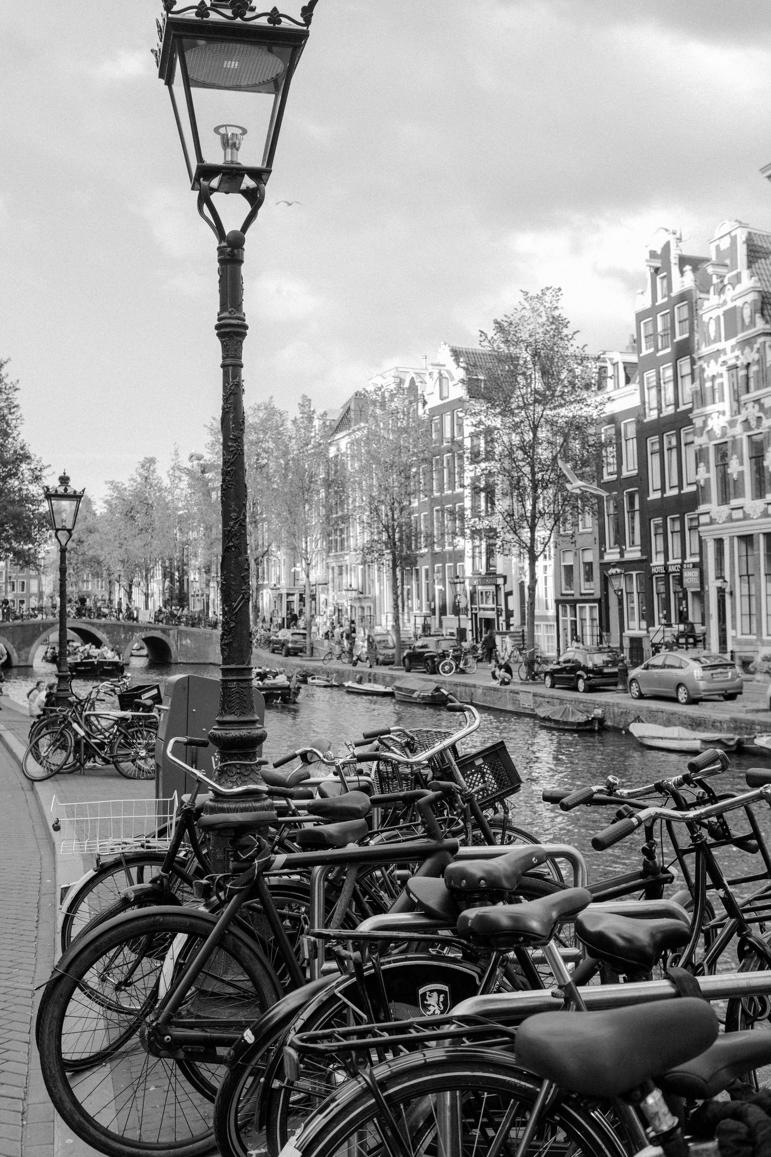 Black and white image of bicycles parked along a canal with a light pole in Amsterdam
